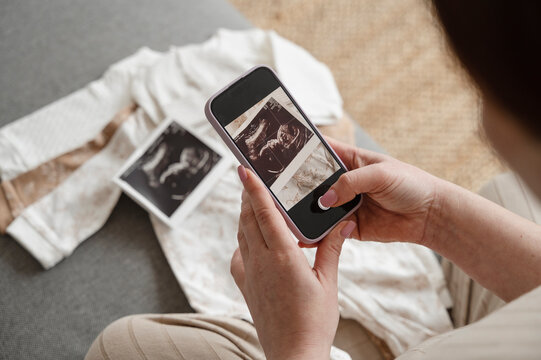 Pregnant woman taking picture of ultrasound through smart phone at home