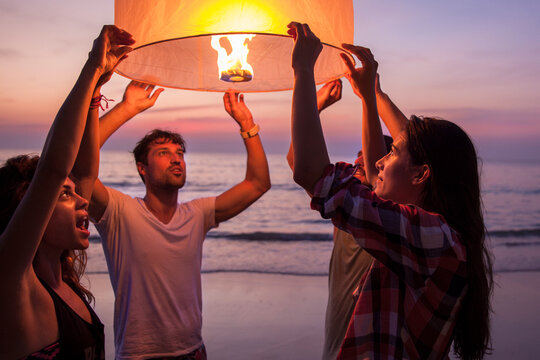 Friends holding lit paper lantern at beach