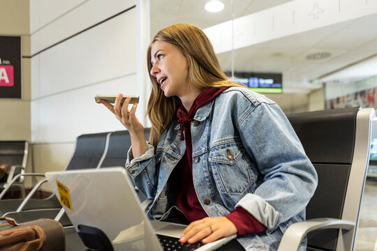 Young woman talking on speaker phone at airport lobby