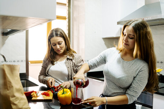 Daughter helping mother preparing food in kitchen at home