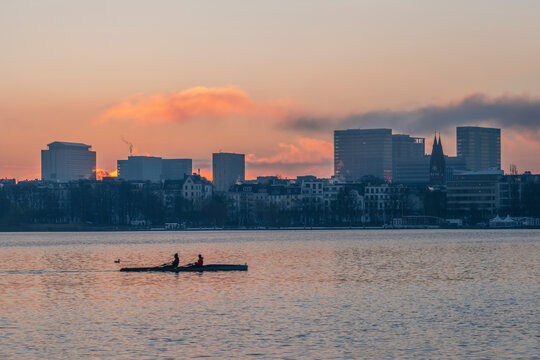 Germany, Hamburg, Alster Lake at dawn with city skyline and rowing boat in background