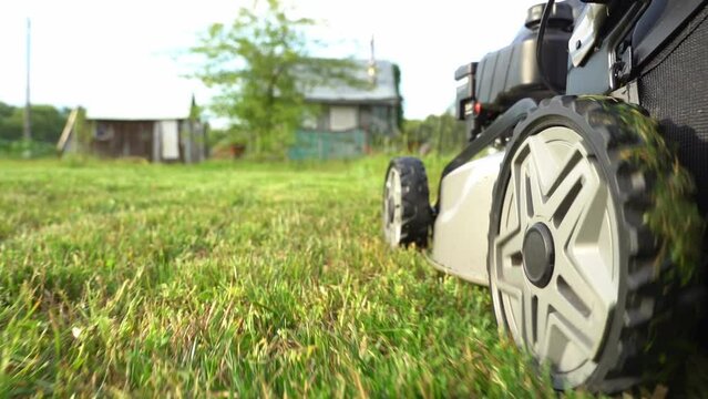 Close up shot of A man mows the grass in the backyard with an electric lawn mower. Slow motion