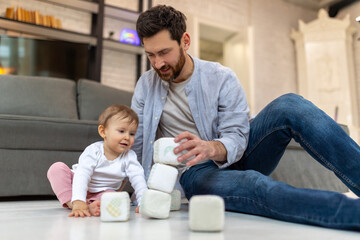 Obraz premium Bearded father playing with toddler child on floor with cubes.