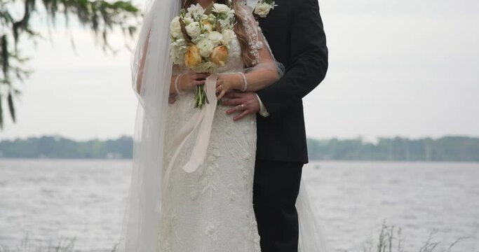 Bride and Groom posing in front of a lake front with her flowers in front of her