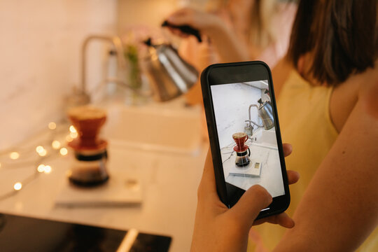 Woman photographing filter coffee through smart phone at home