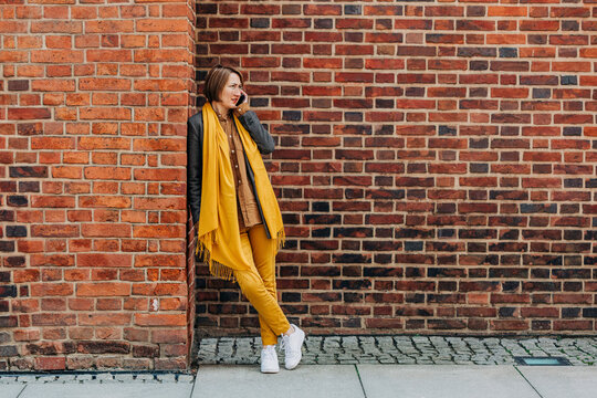 Woman leaning and talking on smart phone by brick wall