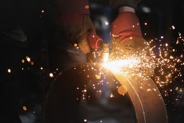 Welder cuts a metal pipe with a plasma cutter close up.