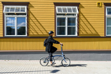 Fototapeta premium Woman in helmet riding on bicycle at city near wooden building