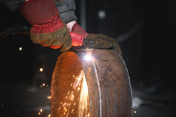 Welder cuts a metal pipe with a plasma cutter close up.
