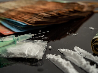 Syringe for injection and cocaine powder, on a black background.