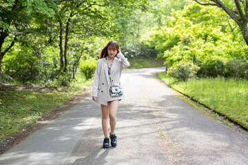 A young Japanese woman in her twenties, wearing a white jacket and shorts, walking through a forest in a large nature park in Hakui City, Ishikawa Prefecture.