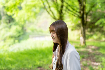 A young Japanese woman in her twenties, wearing a white jacket and shorts, walking through a forest in a large nature park in Hakui City, Ishikawa Prefecture.