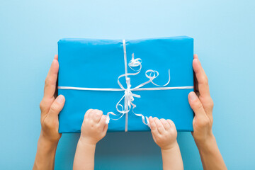 Mother hands giving big wrapped gift. Baby boy fingers touching ribbons and opening paper box. Blue...