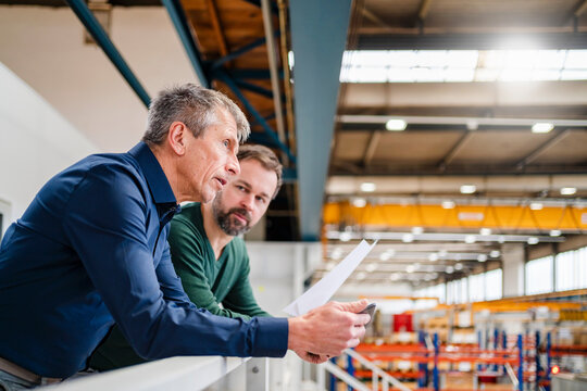 Businessman and manager discussing over document leaning on railing at factory