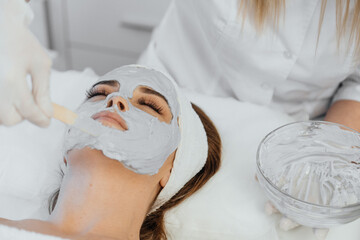 Obraz na płótnie Canvas Applying cosmetics to your face as a simple and effective way to keep your skin young and healthy. Beautiful woman rests during the cosmetic procedure of applying a mask on her face in a beauty salon