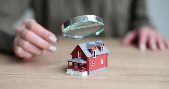 Appraiser is holding magnifying glass and examining miniature of house. Home appraisal and sale
