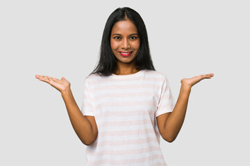 Young Indian woman cut out isolated on white background makes scale with arms, feels happy and confident.