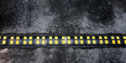 black speed bump with yellow marking located on grey asphalt road at white line under bright sunlight on summer day