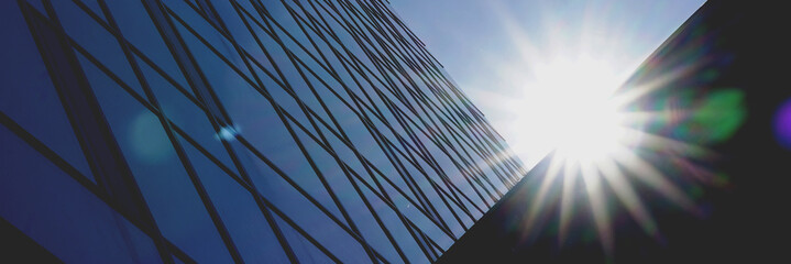 corporate city building with panoramic windows on wall silhouette lit by bright sun under blue sky...