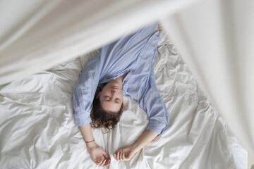 Portrait og beautiful natural looking brunette woman in blue cotton pajama shirt laying on the bed	
