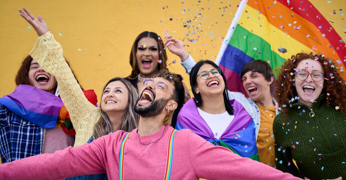 Excited young friends of LGBT community celebrating gay pride day festival. Group of diverse joyful cheerful people having fun together under shower of confetti. Generation z and social event. 