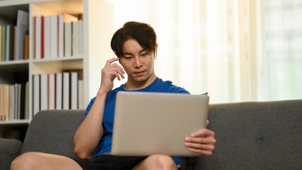 Handsome asian man using laptop, surfing social media, watching movies on couch at home