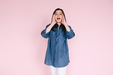 Portrait of young woman with joyous expression, hands near open mouth as if sharing news or telling...