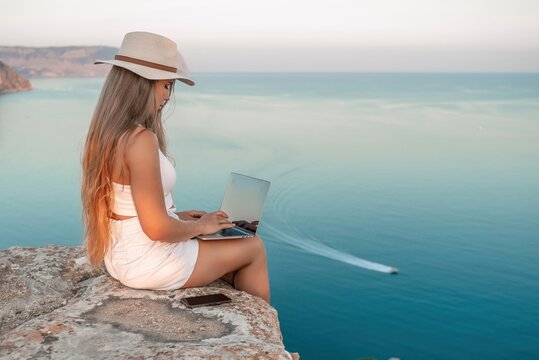 Freelance women sea working on the computer. Good looking middle aged woman typing on a laptop keyboard outdoors with a beautiful sea view. The concept of remote work.