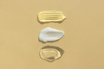 Smears of yellow, white cream and transparent gel or serum on a beige background. The texture of a cosmetic skin care product. Top view.