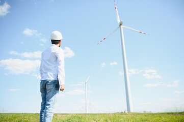Fototapeta na wymiar Portrait of focused indian man standing on field with wind turbines
