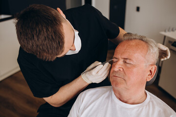 a plastic surgeon measures the face of an elderly man