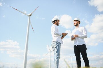 A team of male engineers working together at wind turbine generator farm.