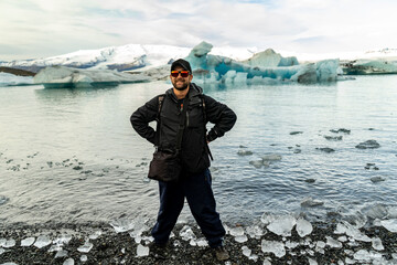 Fototapeta na wymiar smiling man on the shore of Jökulsárlón glacial lagoon with blue icebergs on background