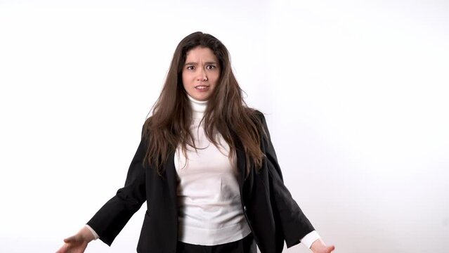 Smartly dressed young woman against white background looking furious while repeatedly rising and dropping arms and shaking head with long dark hair in anger 