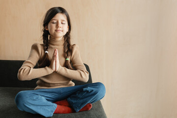 a child of 7 years old sits in a lotus position on a green sofa meditative pose, inside