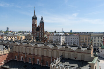 Fototapeta premium St. Mary's Basilica at the Main Market Square in the Old Town district of Krakow, Poland. Aerial view of Bazylika Mariacka or Kościół Mariacki Church Kraków, seen behind Cracow Cloth Hall Sukiennice.