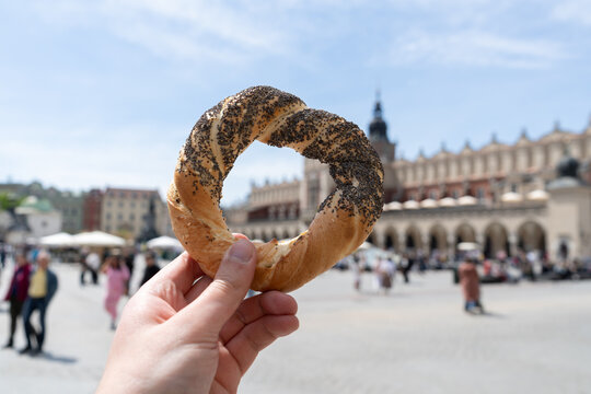 Hand holding obwarzanek krakowski prezel on Krak&oacute;w Main Market Square, with Cracow Cloth Hall Sukiennice in background. Krakowskie obwarzanki, traditional polish snack in Krakow, Poland.