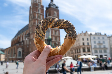 Hand holding obwarzanek krakowski prezel on Cracow Main Market Square. St. Mary's Basilica, Bazylika Mariacka Kraków or Kościół Mariacki Church in bg. Krakowskie obwarzanki food in Krakow, Poland.