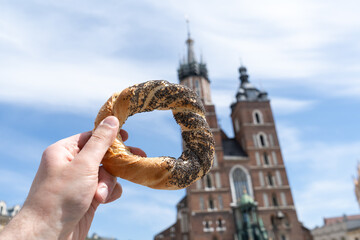 Hand holding obwarzanek krakowski pretzel on Cracow Main Market Square. St. Mary's Basilica,...
