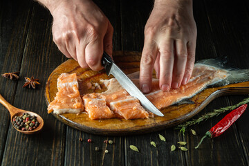 The cook prepares fresh trout fish. Preparing to cook fish food. The cook cuts with knife a red fish before roast.