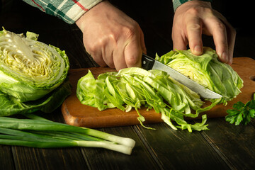 The hands of the cook cut fresh green cabbage on a cutting board with a knife. Close-up of a chef hands while working on a kitchen table. Vegetarian or vegetable diet idea