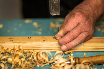 This photo shows a carpenter hammering a nail into a piece of wood with one finger missing, highlighting the risks and dedication required for woodworking jobs. The image represents hard work, courage