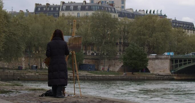 Female street art painter has some sketch practice with Paris city landscape. Experienced European woman artist draws new painting near the river. Painter and her lifestyle hobby leisure