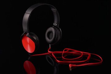 Black headphones with red inserts and a red wire on a black background,