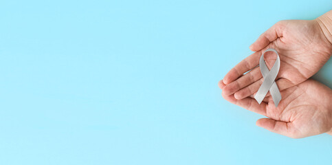World Brain Tumor day. Person's hands are holding a gray ribbon on blue background. This is observed every year on June 8th.