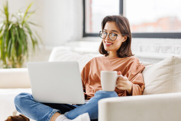 Fototapeta premium young beautiful woman drinking delicious hot coffee while surfing internet at laptop at home
