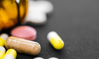 Pile of different prescription pills with pill bottle on black table.