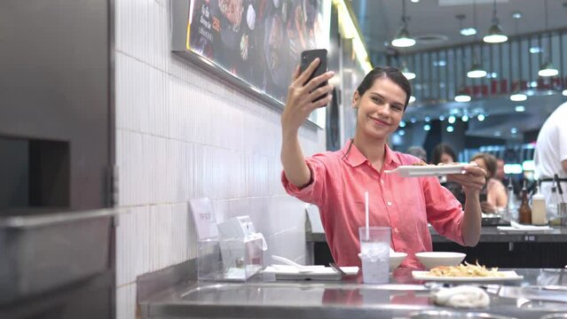 Happy young woman taking selfie enjoying food time and drink in restaurant.