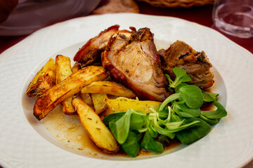 Roast pork meat with baked potato and salad leaves.  Italian dish. Close-up.
