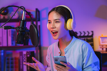 Cheerful beautiful Asian woman wearing headphones and using laptop record podcast at night. Content...
